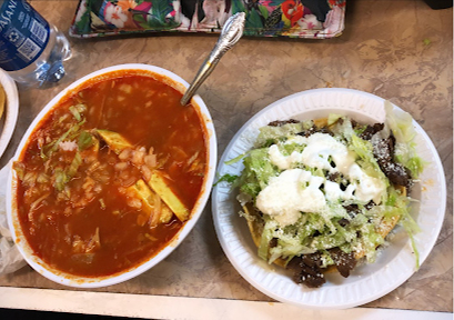 A bright red soupy dish next to tostada topped with fresh lettuce, black beans, and sauce