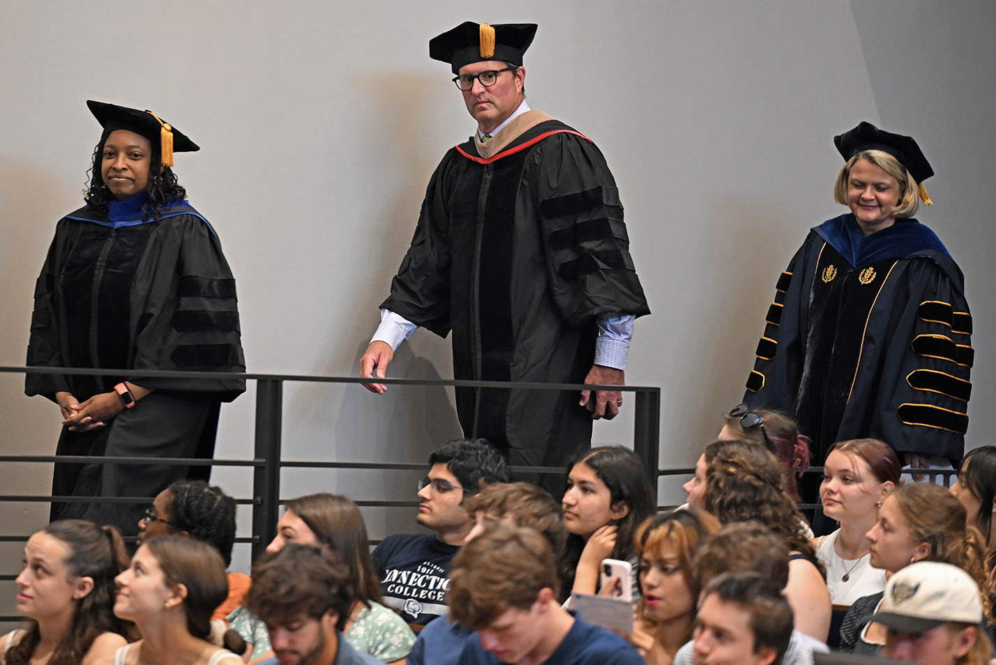 Three administrators in academic regalia process past seated students.