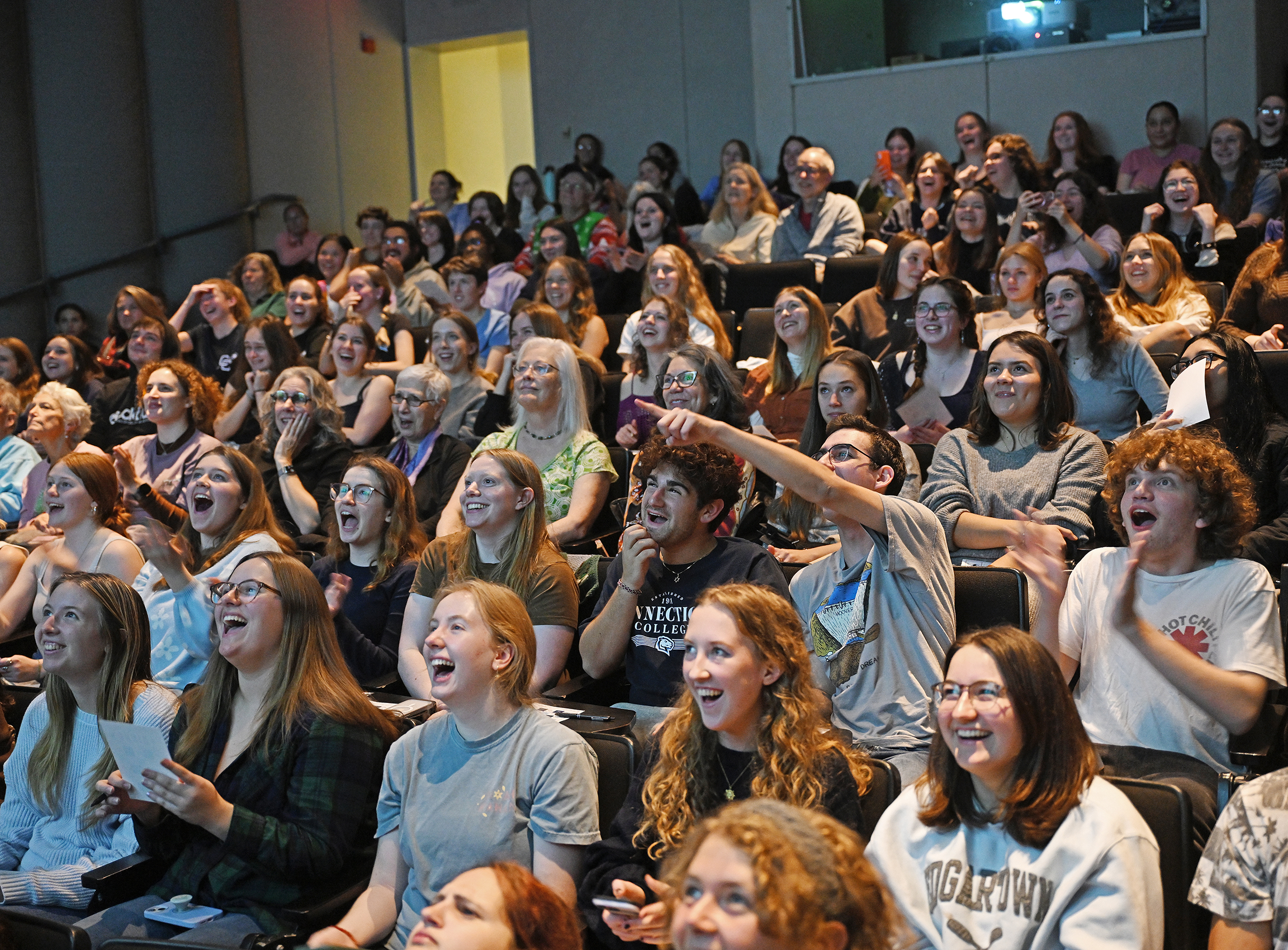 An auditorium full of students laughs and gestures as they watch the premier of a movie filmed on campus.