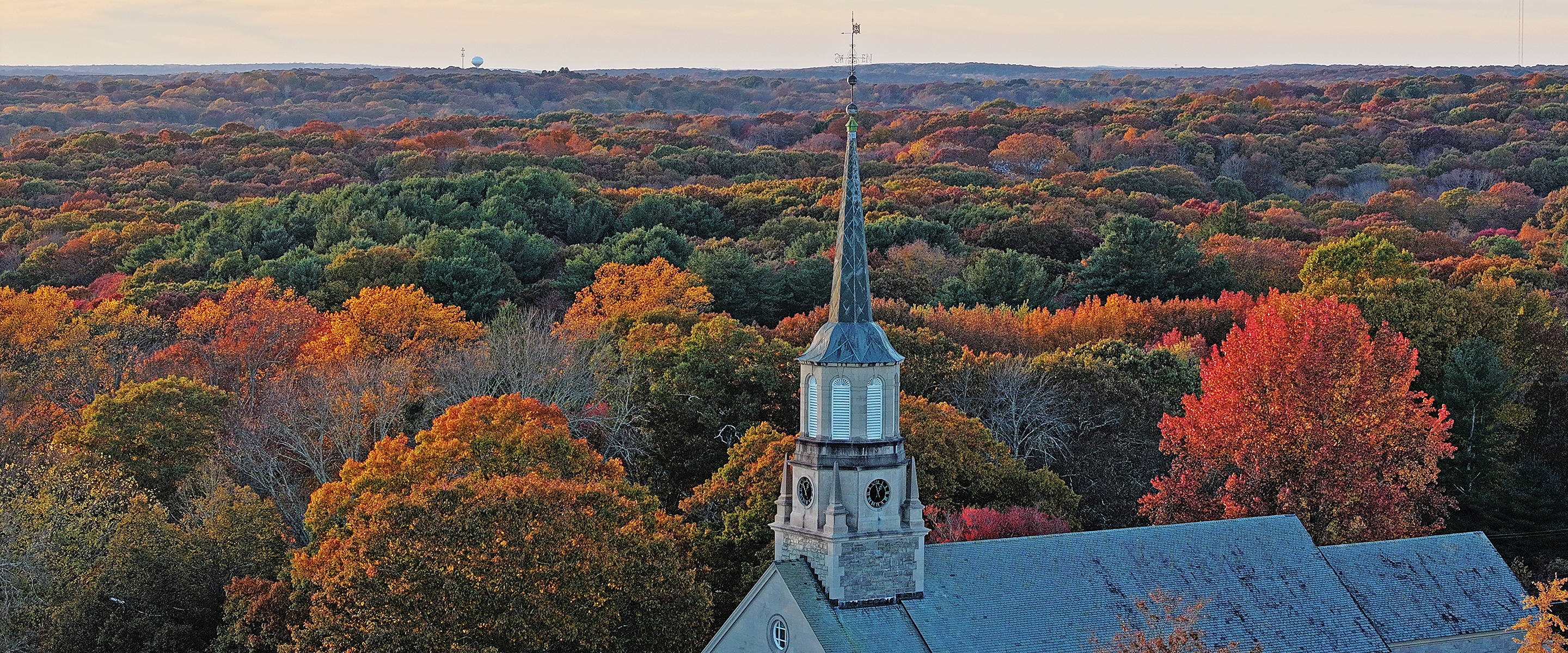 A chapel steeple stands out in front of a panorama of fall foliage color.