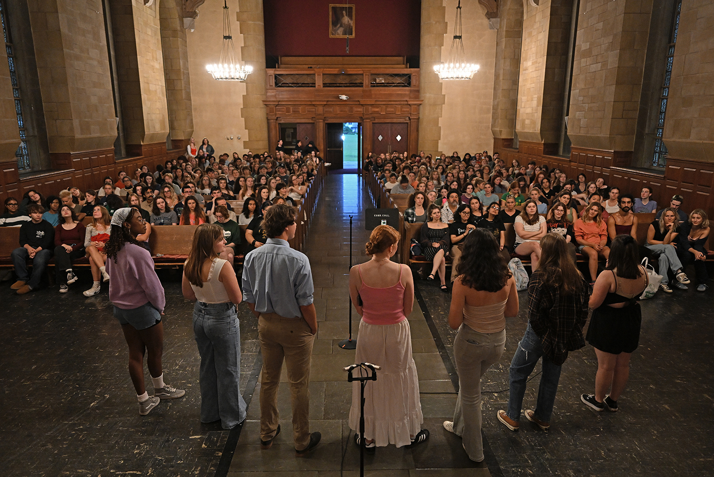 A group of students stand in front of a packed house crowd in a church santuary.