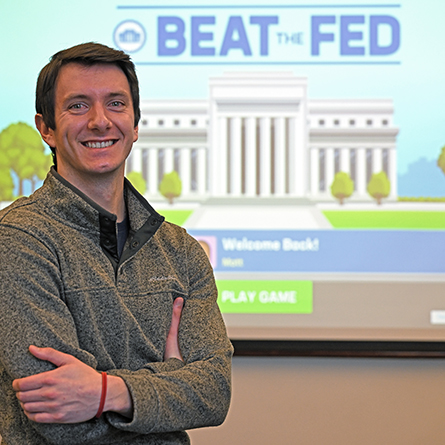 A portrait of Matt Sambor '22 in front of the Beat the Fed game projected in a Fanning Classroom.